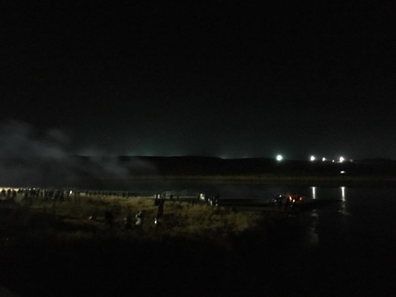 Police on left; water protectors huddled around fires for warmth; DAPL lights on right